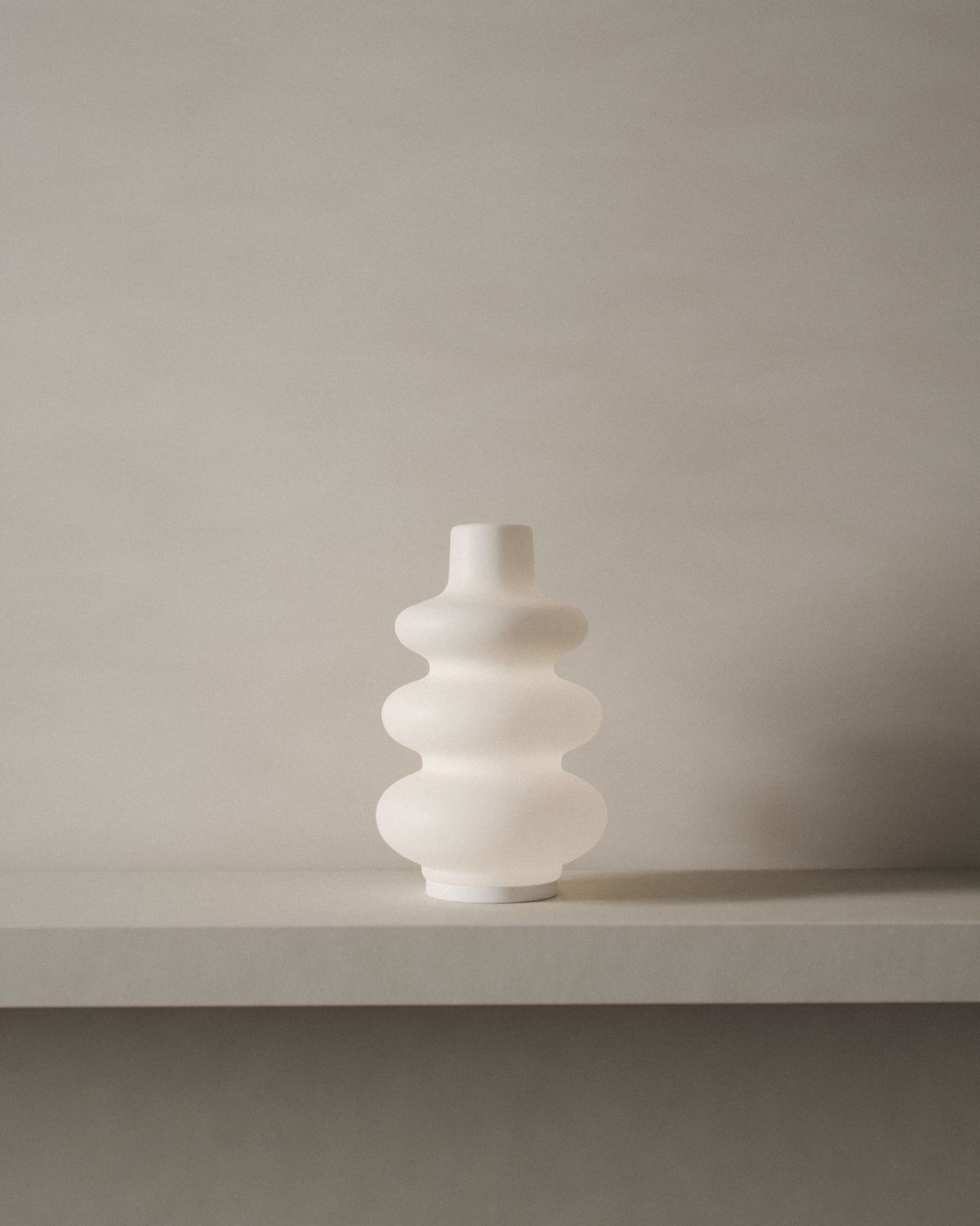 A render of the white glass diffuser glowing softly on a limestone shelf against limewashed plaster, in quiet daylight from a window