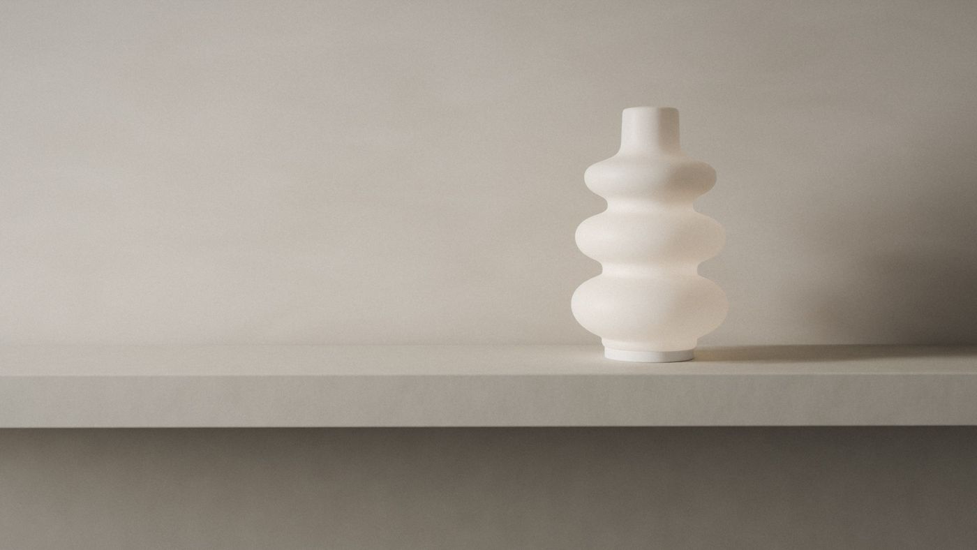 A render of the diffuser alone on a limestone mantel against raw plaster, three soft curves of thick white glass on a slim white base, in low side light