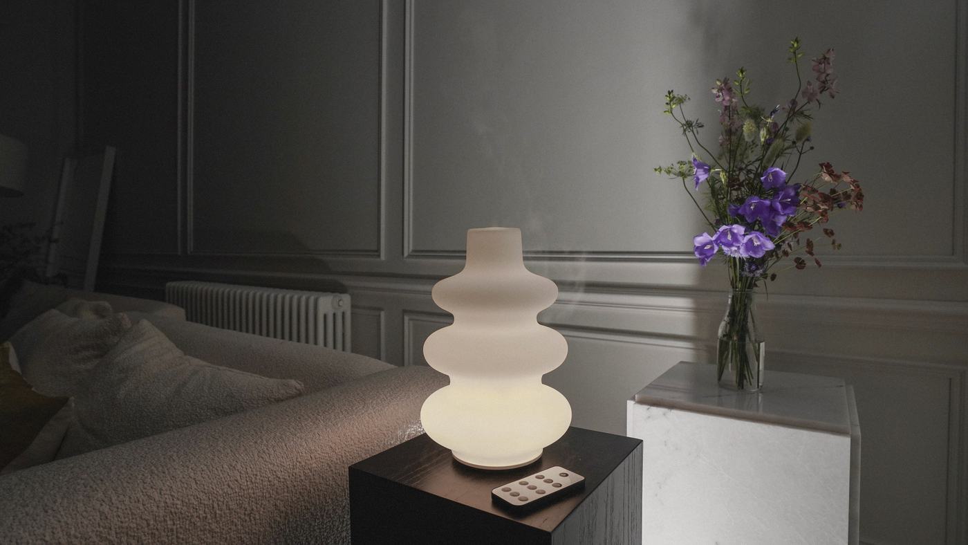 The diffuser glowing softly on a side table at night, its remote beside it